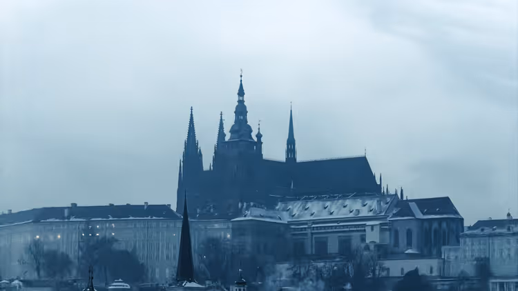 Prager Burg und die Türme des Veitsdoms über leicht verschneiten Dächern an einem grauen, nebligen Wintertag