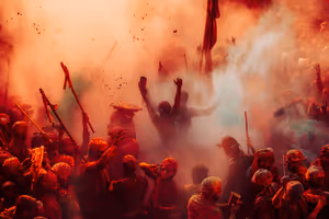 Holi-Feiernde mit Turbanen in Indien heben Stöcke und Arme inmitten dichter Wolken aus rotem und orangem Farbpulver