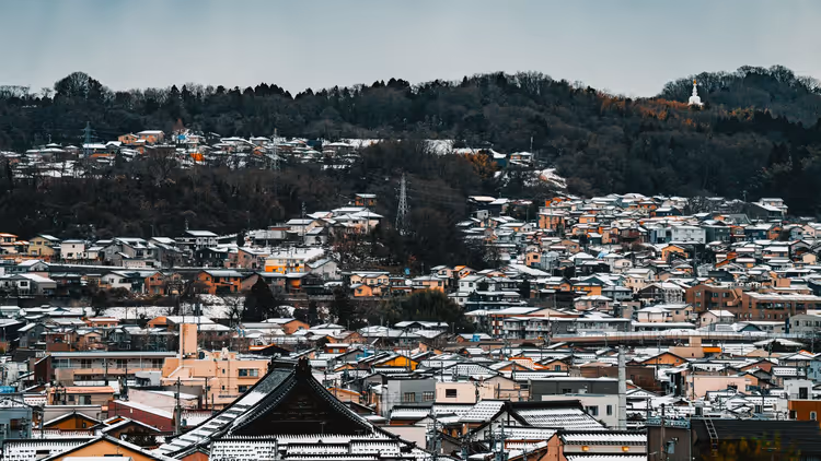 Verschneite japanische Stadt mit Ziegeldächern und Hügeln