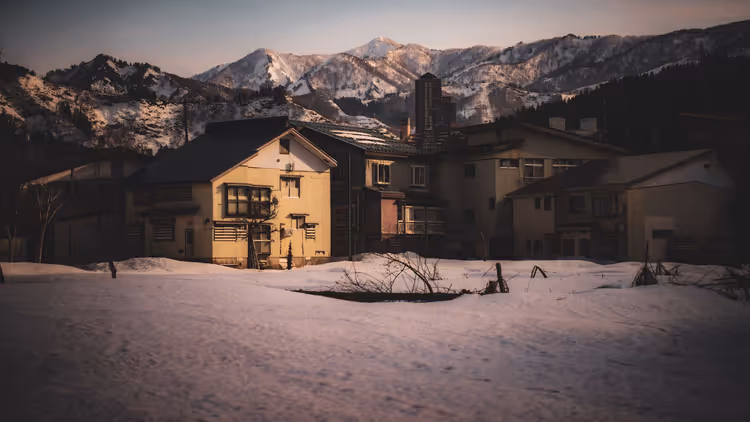 Verschneites Dorf nahe den Bergen in der Abenddämmerung