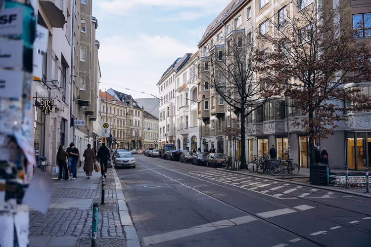 Ruhige Berliner Straße mit Straßenbahngleisen, parkenden Autos, kahlen Bäumen und Fußgängern vor Altbauten