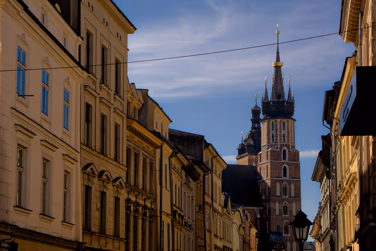 Backsteingotischer Turm der Marienkirche ragt über sonnenbeschienene Fassaden der Bürgerhäuser in Krakau