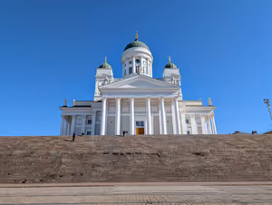 Weißer klassizistischer Dom von Helsinki mit grünen Kuppeln über einer breiten Steintreppe unter klarem blauem Himmel