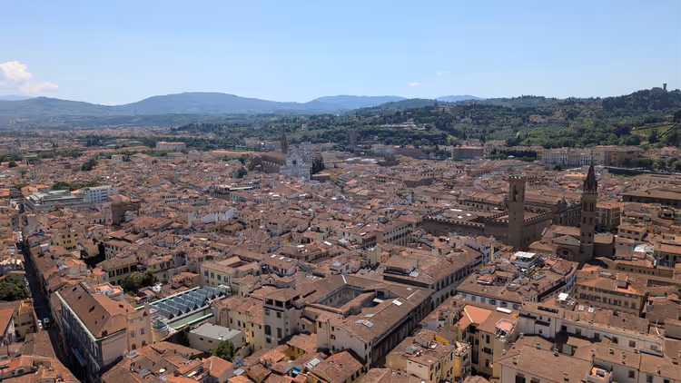 Terrakottadächer von Florenz von oben, mit Kirchtürmen und grünen Hügeln am Horizont