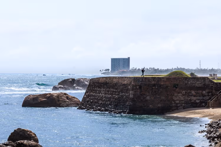 Steinerne Bastion des Forts von Galle über dem Indischen Ozean, ein einzelner Spaziergänger auf dem Wall und Felsen in der Brandung, Sri Lanka