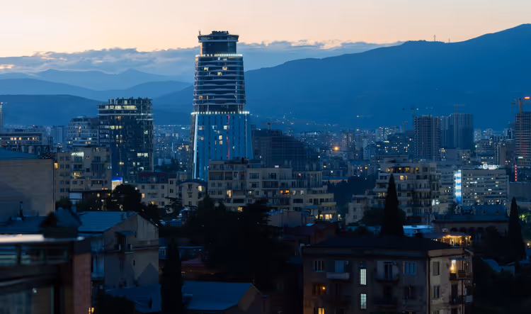 Avondpanorama van Tbilisi met een hoogbouw tegen de bergen