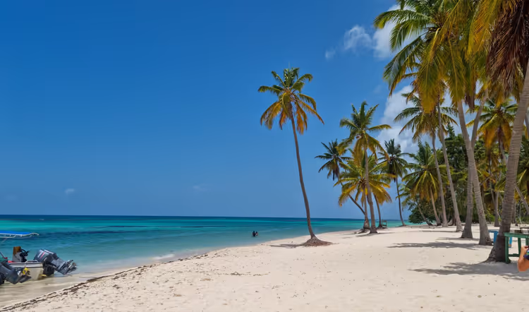 Weißer Sandstrand mit hohen Kokospalmen an ruhigem türkisfarbenem Meer, am Ufer liegen Boote