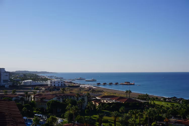 Küste von Belek von oben mit palmenreichen Hotelgärten, roten Dächern und Stegen, die ins ruhige blaue Meer reichen