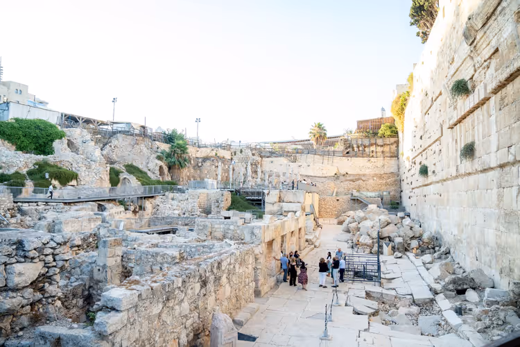 Besucher zwischen freigelegten Steinruinen neben einer hoch aufragenden antiken Kalksteinmauer in Jerusalem
