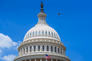 Witte koepel van het Capitool in Washington tegen een diepblauwe lucht, met een Amerikaanse vlag eronder en een passerend straalvliegtuig