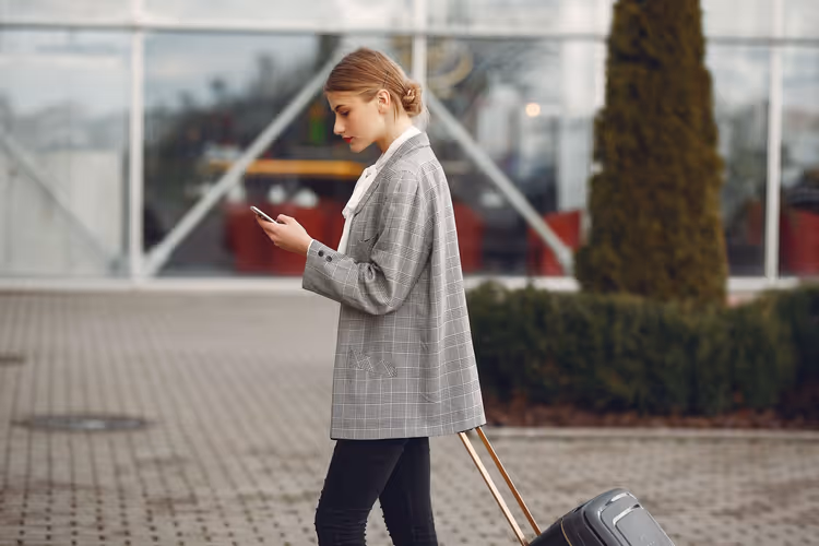 Dziewczyna z walizką i smartfonem przy nowoczesnym budynku
