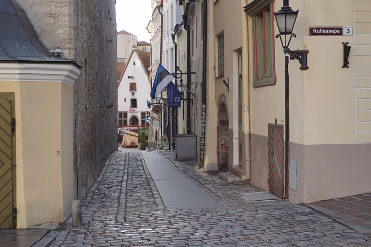 Schmale Kopfsteinpflastergasse in der Altstadt von Tallinn mit pastellfarbenen Häusern, estnischer Flagge und alter schmiedeeiserner Laterne