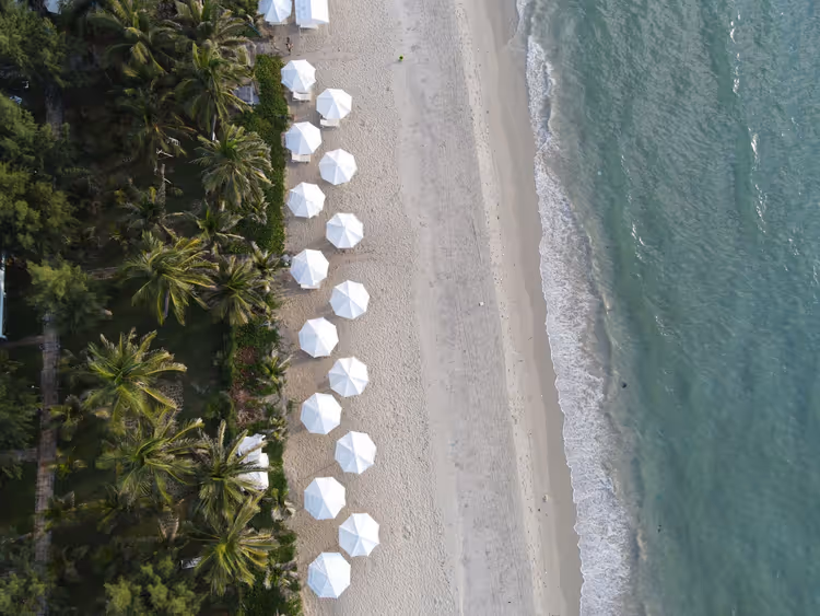 Witte parasols en ligstoelen op een zandstrand van bovenaf