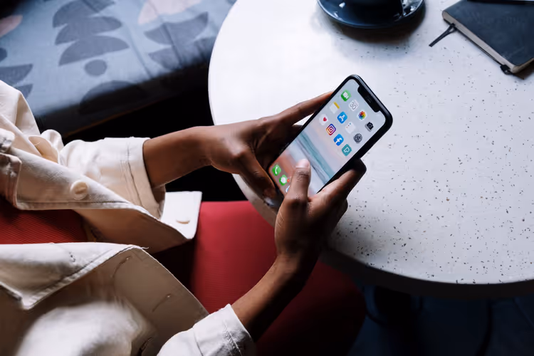 Osoba trzyma smartfon z aplikacjami przy stoliku w kawiarni