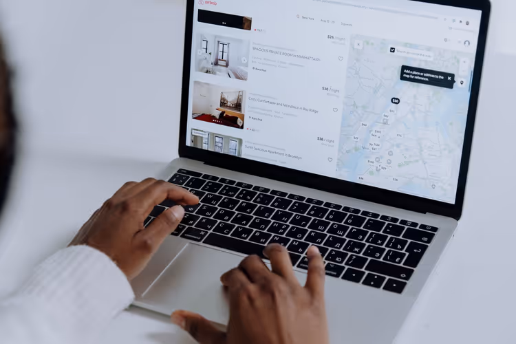 Handen typen op een laptop, zoeken naar accommodatie op een kaart