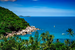 Türkisfarbene Bucht auf Koh Samui mit dschungelbewachsener Landzunge, Granitfelsen, Kokospalmen und einem weißen Schnellboot