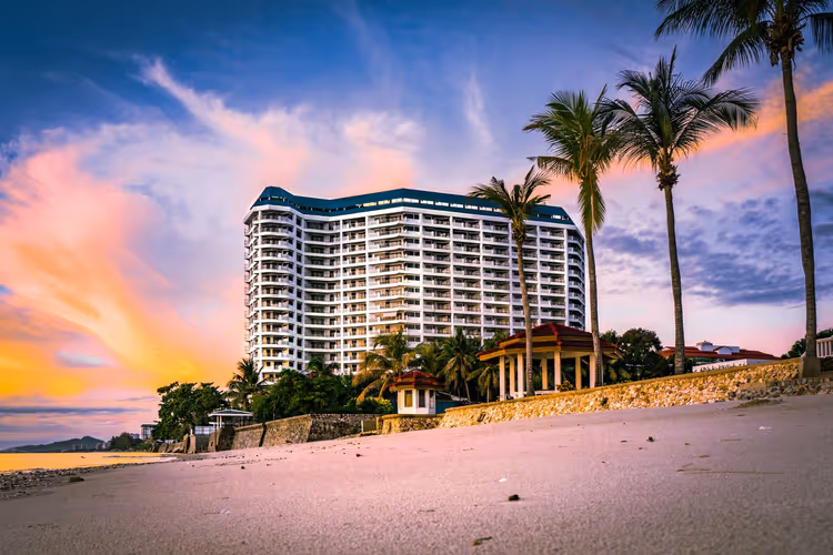 Wit hotel aan het strand met palmbomen bij zonsondergang