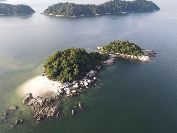 Veduta aerea di isolotti boscosi con massi di granito e una lingua di sabbia bianca in un mare verde e calmo in Malesia