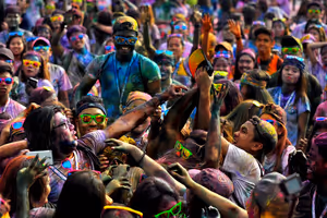 Gęsty tłum młodych ludzi w neonowych okularach, obsypanych kolorowym proszkiem, wyciąga do siebie ręce na imprezie Holi