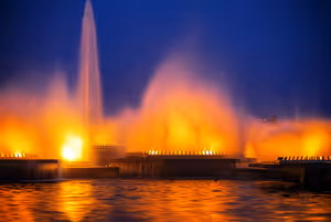 Beleuchtete Fontänen leuchten nachts orange über dunklem Wasser bei der Show des Roshen-Springbrunnens in Winnyzja