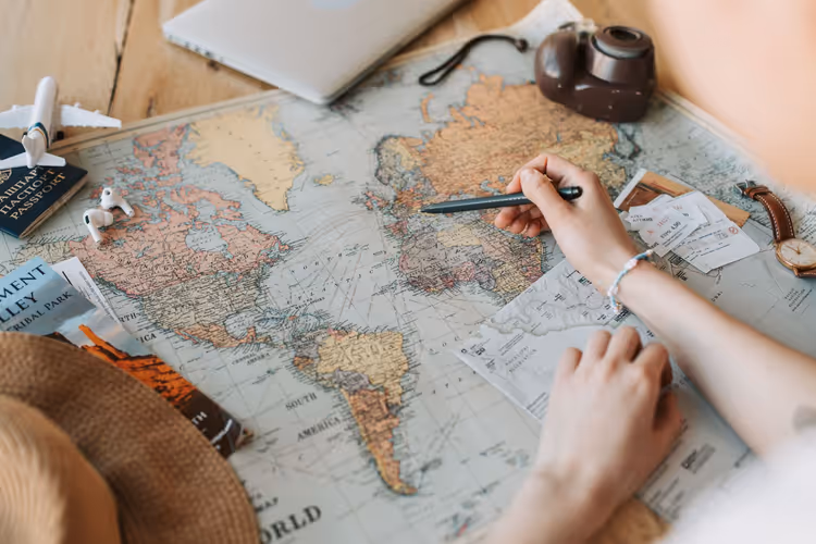 Handen markeren een route op een wereldkaart met tickets en een paspoort