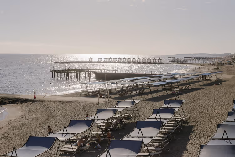 Strand met ligstoelen en pier bij zonsondergang