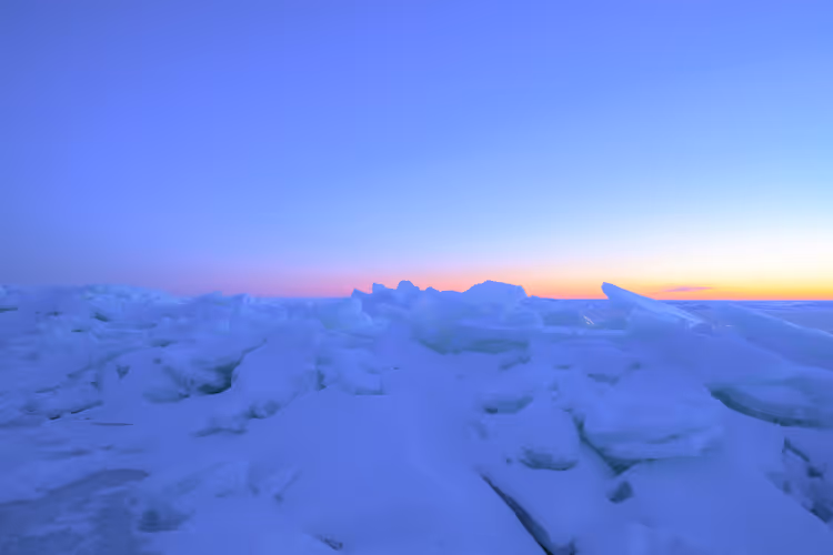 Zerklüftetes Packeis im blauen Dämmerlicht mit einem orange und rosa leuchtenden Streifen am Horizont