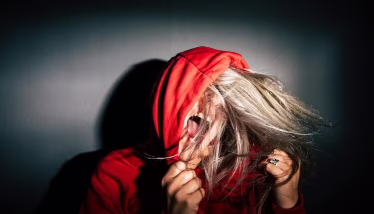 A teenager in a red hoodie screams with hair flying, conveying intense emotion.