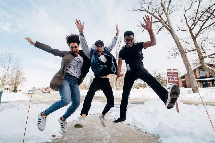 Drei Freunde springen fröhlich im Schnee – Momentaufnahme mit Bewegungsdynamik Junge Menschen springen lachend in die Luft an einem verschneiten Wintertag, festgehalten in einer actionreichen Fotosequenz