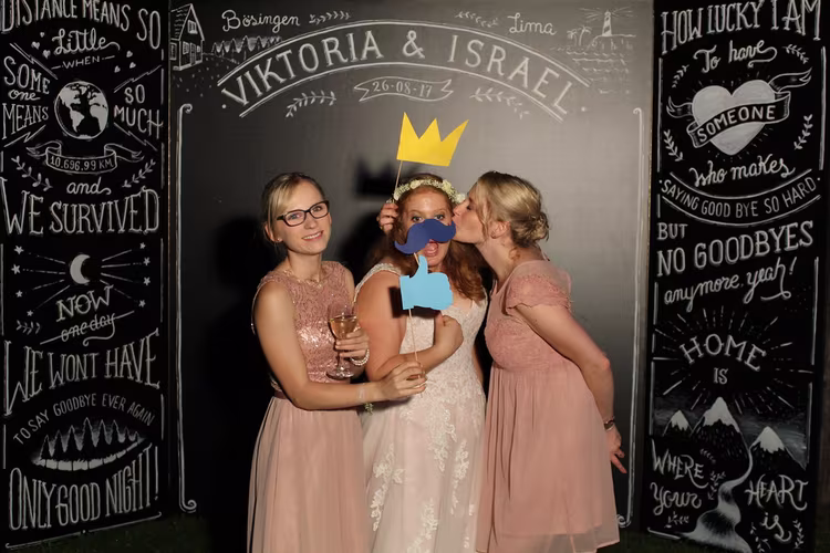 Fotobox-Spaß bei einer Hochzeit mit kreativen Requisiten und Freundinnen Drei Frauen in festlicher Kleidung posieren in einer Fotobox auf einer Hochzeit, mit lustigen Requisiten wie Krone und Schnurrbart