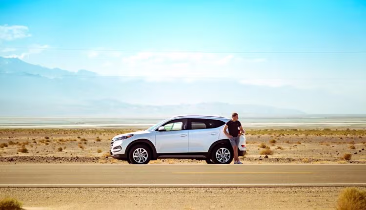 man standing beside white SUV near concrete road under blue sky at daytime